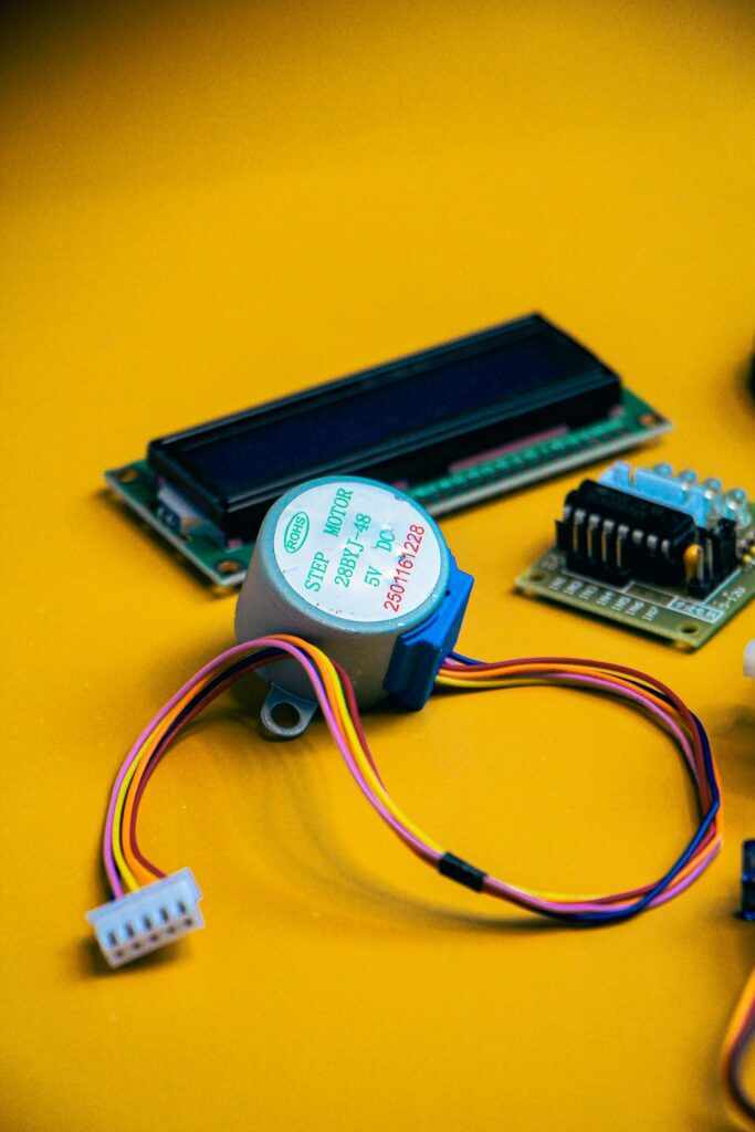 pexels photo 35673112 35673112 Close-up of electronic components including a step motor and circuit board on a vibrant yellow background.