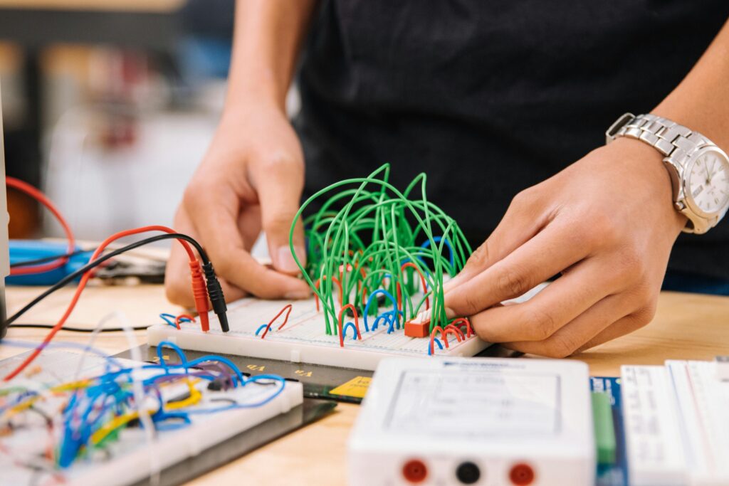 Hands manipulating wires on breadboards for electronic prototyping.
